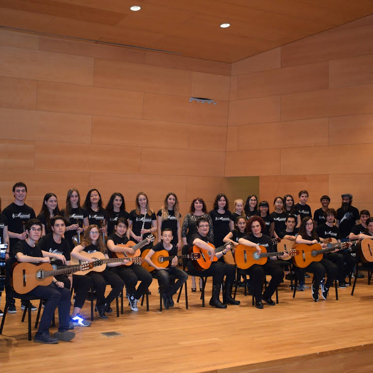Foto de família d'un concert a l'Auditori de Santa Coloma de Gramenet. Surten guitarristes seguts a davant, i altres músics darrere (flautes, violinistes, pianistes, etc.).